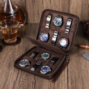 May include: A brown leather watch roll with eight slots for storing watches. The roll is open and shows several watches with different colored faces and bands.
