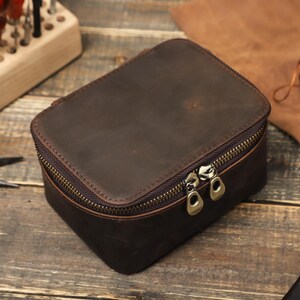May include: A brown leather travel case with a zipper closure. The case has two zipper pulls and is made of distressed leather.