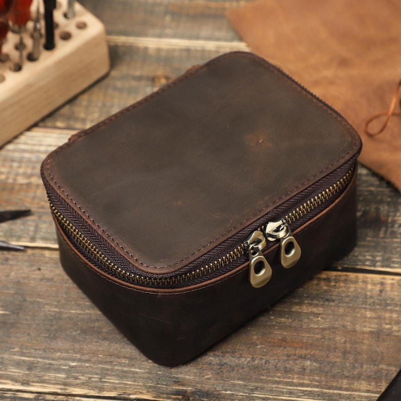 May include: A brown leather travel case with a zipper closure. The case has two zipper pulls and is made of distressed leather.