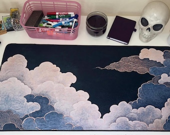 May include: A rectangular desk mat featuring a dark navy blue background with stylized, layered clouds in shades of light pink, white, and muted blue. The cloud patterns include intricate, fine-lined circular textures throughout the design.
