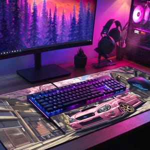 Op de afbeelding: Een gaming-opstelling met een desktopcomputer, monitor, toetsenbord, muis en headset. Het bureau heeft een grote muismat met een roze autografiek. Het toetsenbord en de computer hebben kleurrijke LED-verlichting. Een kleine plant in een pot staat op het bureau.