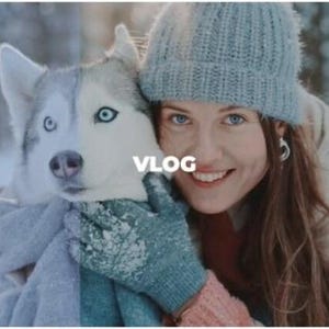 May include: A woman and a husky dog are embracing in a snowy outdoor setting. The woman wears a blue knit cap, a white jacket, and mittens. The dog has striking blue eyes. The word "VLOG" is superimposed on the image.