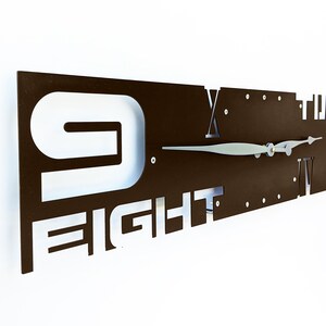 May include: A brown metal wall clock with white numbers and the word "FIGHT" in the design. The clock hands are silver.