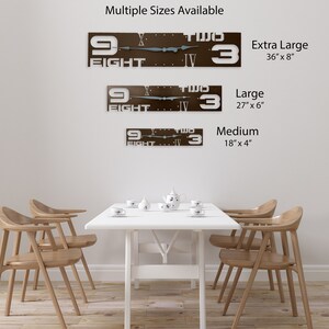 May include: A brown metal clock with white Roman numerals and white numbers. The clock face says "Nine Two Three" and "Eight Four". The clock is available in three sizes: Extra Large (36 inches by 8 inches), Large (27 inches by 6 inches), and Medium (18 inches by 4 inches).