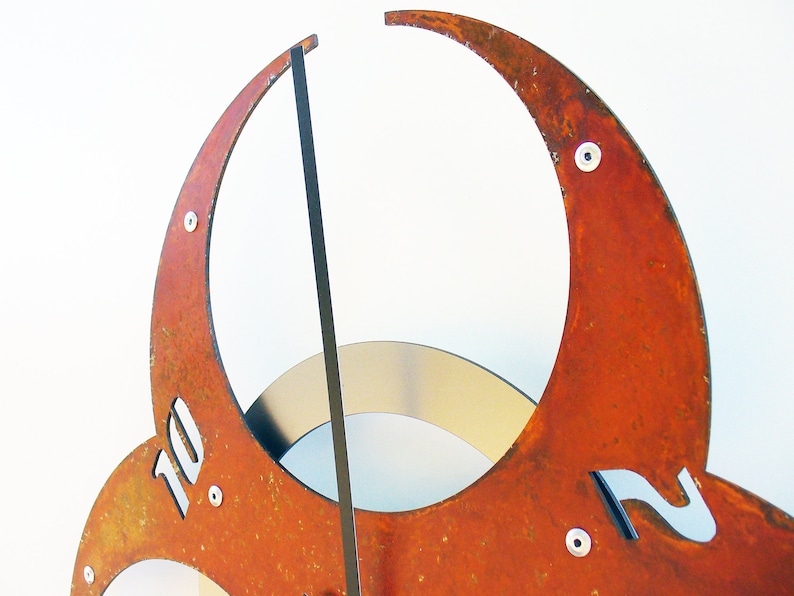 May include: A rusty metal clock with Roman numeral markings. The clock face is made of three overlapping crescent shapes. The clock hands are black.