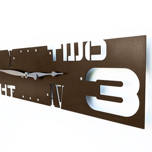 May include: A brown metal wall clock with white Roman numeral and Arabic numeral hour markers. The clock face is surrounded by the words "FIGHT" and "TWO". The clock hands are silver.