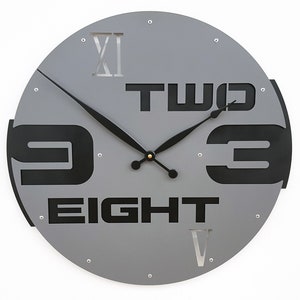 May include: Gray round wall clock with black Roman numeral XII and black numbers 'TWO', 'NINE', 'THREE', and 'EIGHT' on the face.