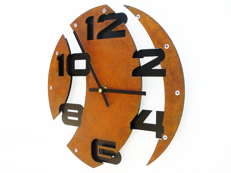 May include: A rusty brown metal wall clock with black numbers and hands. The numbers are arranged in a unique, asymmetrical pattern.