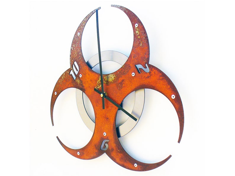 May include: A rusty orange metal wall clock shaped like a biohazard symbol with black clock hands and silver numbers.