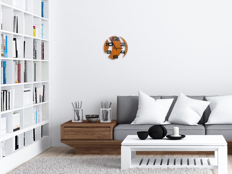 May include: A modern living room with a white bookshelf, a gray sofa with white pillows, a wooden coffee table, and a unique orange clock on the wall.