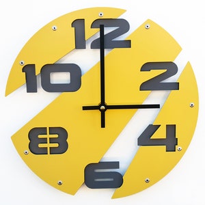 May include: A yellow circular clock with black numbers and hands. The numbers are arranged in a unique pattern, with some numbers partially hidden behind others.