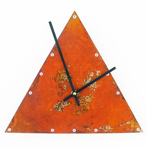 Peut inclure: Horloge murale triangulaire avec un cadran en métal orange rouillé. L'horloge a des aiguilles noires et de petits rivets blancs sur le pourtour. Le cadran de l'horloge a un aspect texturé et vieilli, ajoutant une esthétique industrielle unique.