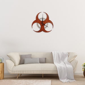 May include: A white couch with a white throw blanket and a brown biohazard symbol clock on the wall above it.