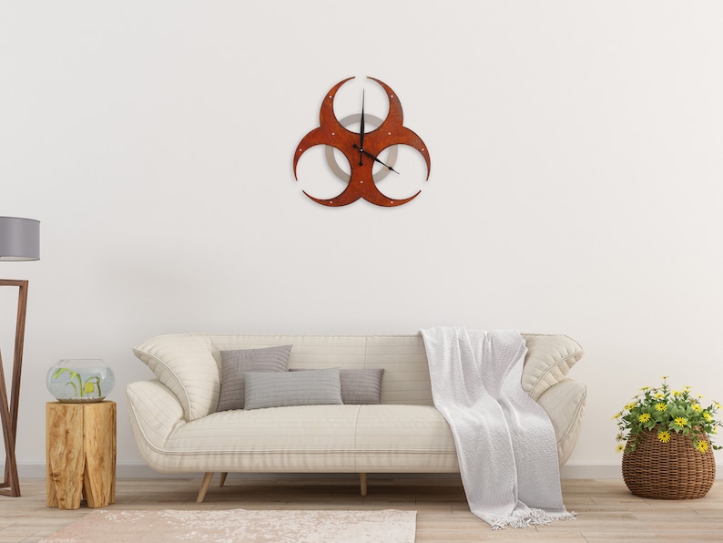 May include: A white couch with a white throw blanket and a brown biohazard symbol clock on the wall above it.