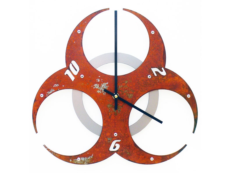 May include: A rusty red metal clock shaped like a biohazard symbol with black hands and white numbers. The clock has a silver inner circle.