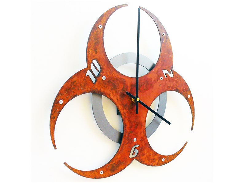 May include: A rusty orange metal wall clock shaped like a biohazard symbol with black hands and silver numbers.