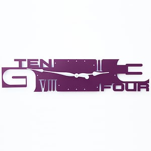 May include: Purple wall clock with white hands and Roman numeral markings. The clock face is shaped like the words "Nine Four Ten".