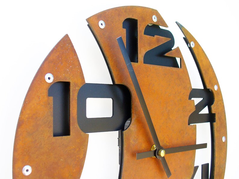 May include: A rusty brown metal clock with black numbers and hands. The clock is designed in a unique, abstract style with the numbers cut out of the metal.