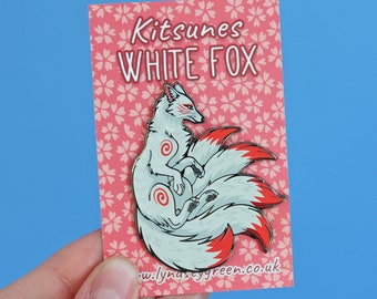 May include: White fox kitsune enamel pin with red and white nine tails. The pin is on a pink background with white cherry blossoms. The text "Kitsunes White Fox" is printed on the card.