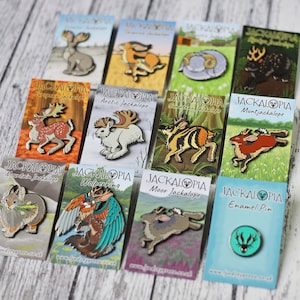 Pode incluir: Uma coleção de 11 pinos de esmalte com diferentes Jackalopes, um coelho mítico com chifres. Cada pino tem um design e um nome únicos, como "Jackalope europeu", "Jackalope ártico" e "Wolperking". Os pinos são exibidos em cartões brancos com o logotipo Jackalope e o endereço do site.