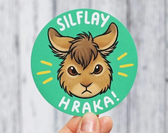 Może przedstawiać: Okrągła naklejka z turkusowym tłem przedstawiająca ilustrację głowy brązowego królika. Królik ma duże uszy i surowy wyraz pyska. Biały napis SILFLAY HRAKA jest wydrukowany w łuk wokół królika, z żółtymi akcentami w formie kresek.