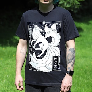 May include: Black t-shirt with a white illustration of a nine-tailed fox, a lantern, and Japanese text. The fox is set in a rectangular frame with a moon and stars. The shirt has short sleeves.