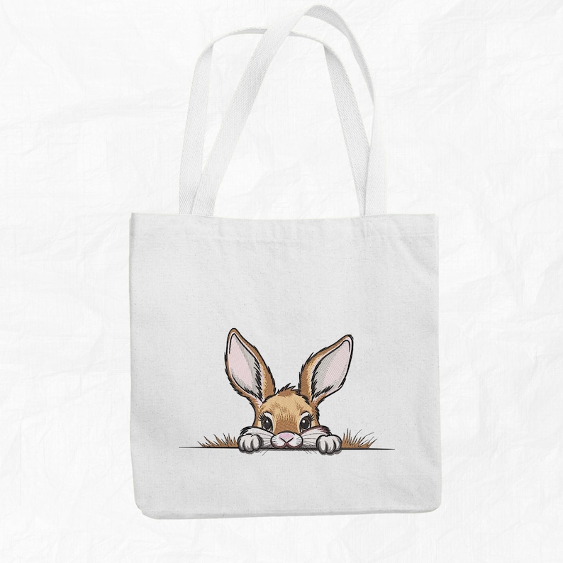May include: White canvas tote bag with a brown rabbit peeking out from behind the top edge. The rabbit has brown fur, long ears, and pink nose.