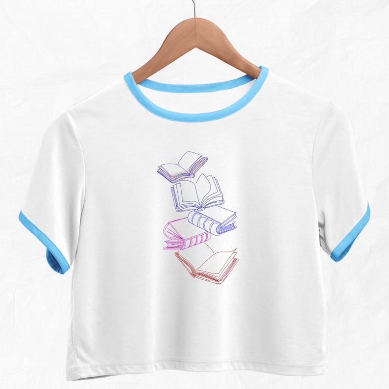 May include: White cropped t-shirt with a blue ringer neckline and a graphic of five books in a gradient of pink and purple.