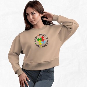 May include: A tan sweatshirt with a colorful puzzle piece design and the words "Love, Understand, Accept, Autism" around the puzzle pieces.