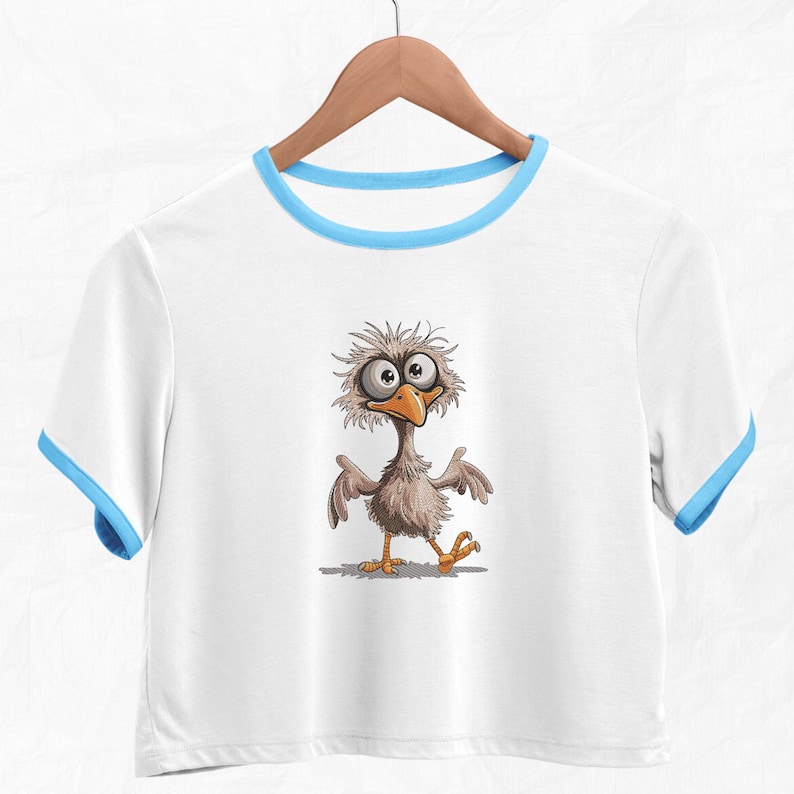 May include: White crop top with a blue trim around the neckline. The shirt features a cartoon illustration of a bird with large eyes and a funny expression.