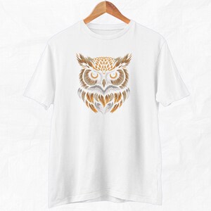 Op de afbeelding: Wit T-shirt met een afbeelding van een uil met bruine en gouden veren. De ogen van de uil zijn geel.