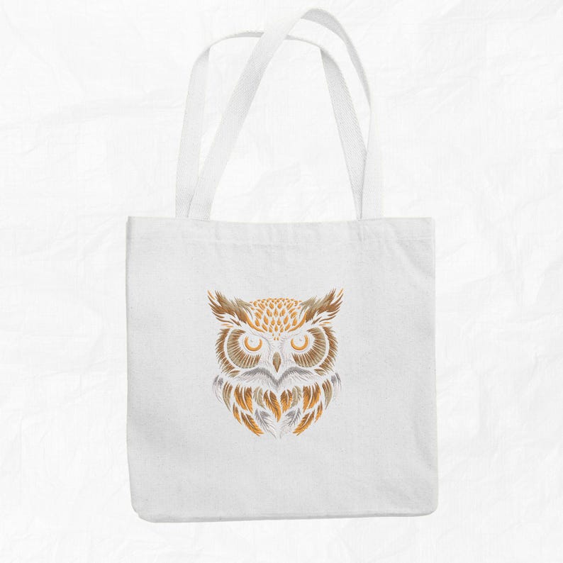 Op de afbeelding: Witte tote bag met een bruin en gouden uil ontwerp. De ogen van de uil zijn groot en zwart, en zijn veren zijn gedetailleerd.
