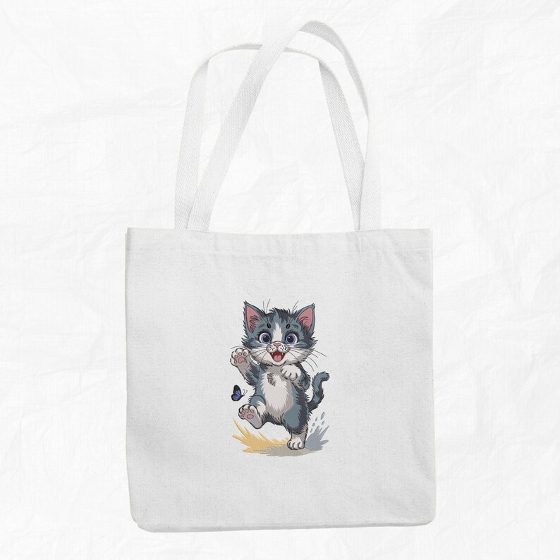 May include: White tote bag with a cartoon image of a grey and white kitten chasing a blue butterfly. The kitten is smiling and has its paw raised. The bag has two white handles.
