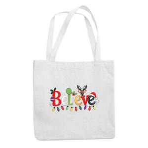 May include: White tote bag with the word "Believe" in colorful, festive lettering. The design includes Christmas lights, a reindeer, and a Santa hat, perfect for holiday shopping or gifting.