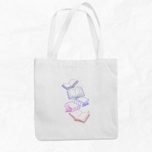 May include: White tote bag with a design of five books in shades of pink and blue, with the books stacked on top of each other and some floating in the air.