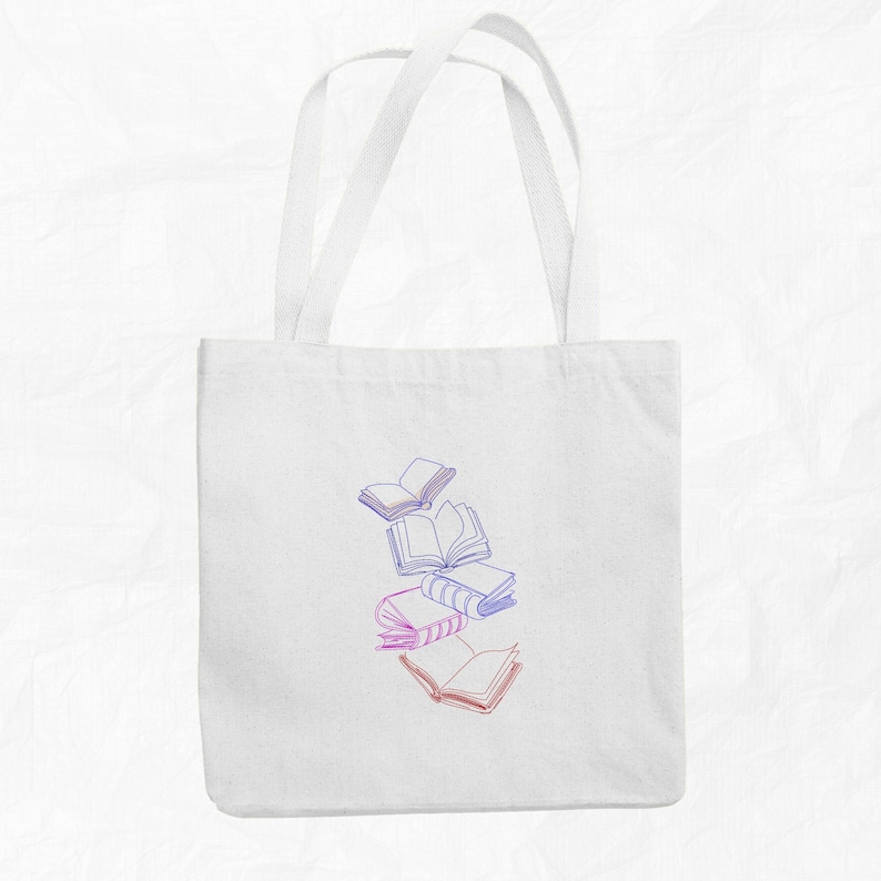 May include: White tote bag with a design of five books in shades of pink and blue, with the books stacked on top of each other and some floating in the air.