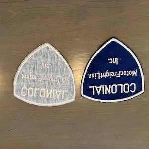 May include: Two triangular patches with white stitching on a blue background. The text on the patches reads "COLONIAL Motor Freight Line Inc."