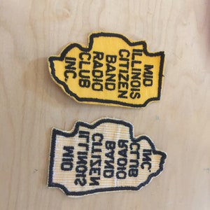 May include: Two yellow embroidered patches shaped like the state of Illinois. The top patch reads "MID ILLINOIS CITIZEN BAND RADIO CLUB INC." The bottom patch reads "MID ILLINOIS CITIZEN BAND RADIO CLUB INC."