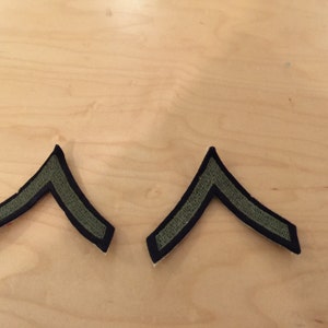 May include: Two dark green and black chevron shaped patches. The patches are made of fabric and have a stitched edge.