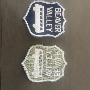 May include: Two embroidered patches in the shape of a shield. The top patch is dark blue with white stitching and the text "BEAVER VALLEY". The bottom patch is white with a light blue mesh background and the text "BEAVER VALLEY" in white.