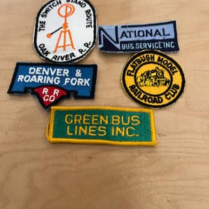 May include: A collection of five embroidered patches featuring various designs and text: The Switch Stand Route Oak River R.R., National Bus Service Inc., Denver & Roaring Fork R.R. Co., Flatbush Model Railroad Club, and Green Bus Lines Inc.