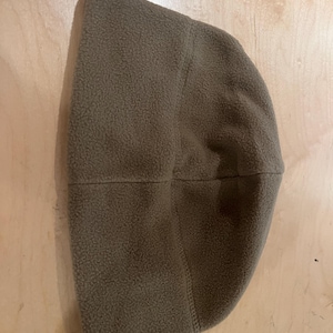 May include: A brown fleece beanie hat. The hat is made of a soft, textured material and has a simple, classic design. The hat is a solid color and appears to be warm and comfortable.