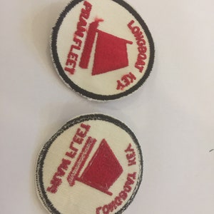 May include: Two white embroidered patches with black outlines. The patches are round and feature a red sailboat with the text "Longboat Key" and "Swim Fleet" on each patch.