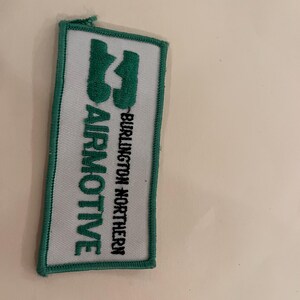 May include: A rectangular patch with a white background and a green border. The patch features the words "AIRMOTIVE" in green and "BURLINGTON NORTHERN" in black. A green graphic is also present.