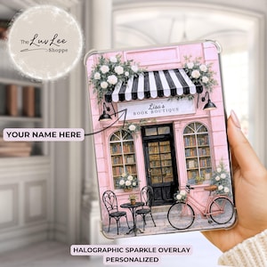 May include: A pink tablet case featuring a watercolor illustration of a bookstore facade with a black and white striped awning. The case has the text "Lisa's Book Boutique" and a pink bicycle. The case is personalized.