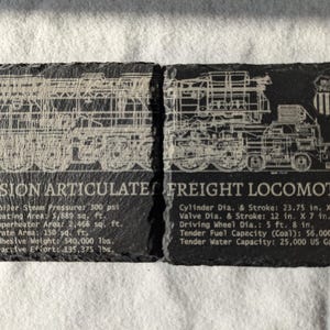 May include: Two black slate coasters with white engraved images of a steam locomotive. The left coaster has the text "Expansion Articulate" and lists the locomotive's specifications. The right coaster has the text "Freight Locomotive" and lists the locomotive's specifications.