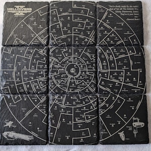 May include: Nine black slate coasters with a white circular map of the galaxy on each. The coasters feature the text "HELLDIVERS XZAR" and a quote from General Brasch: "You're finally ready for the real deal of 'em all. The Galactic War. Liberty, Democracy, Justice. They're in your hands."
