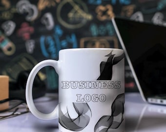 May include: A white ceramic mug with the words "BUSINESS LOGO" in a black, outlined font. The mug features a design of black and grey abstract shapes. A laptop and other office supplies are in the background.