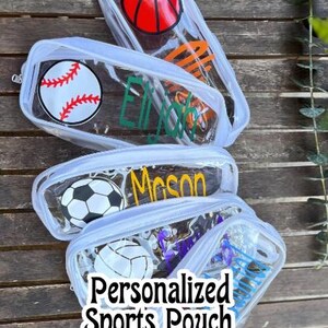 May include: Clear, zippered pouches with sports ball designs, including a basketball, baseball, and soccer ball. The pouches are personalized with names in various colors. The text "Personalized Sports Pouch" is also visible.