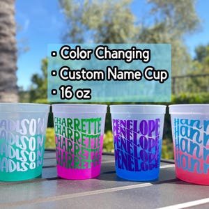 May include: Four 16 oz color-changing plastic cups with custom names printed in repeating patterns. The first cup is teal with white text reading Madison, the second is pink with green text reading Charrette, the third is blue with purple text reading Penelope, and the fourth is red with blue text reading Hannah.